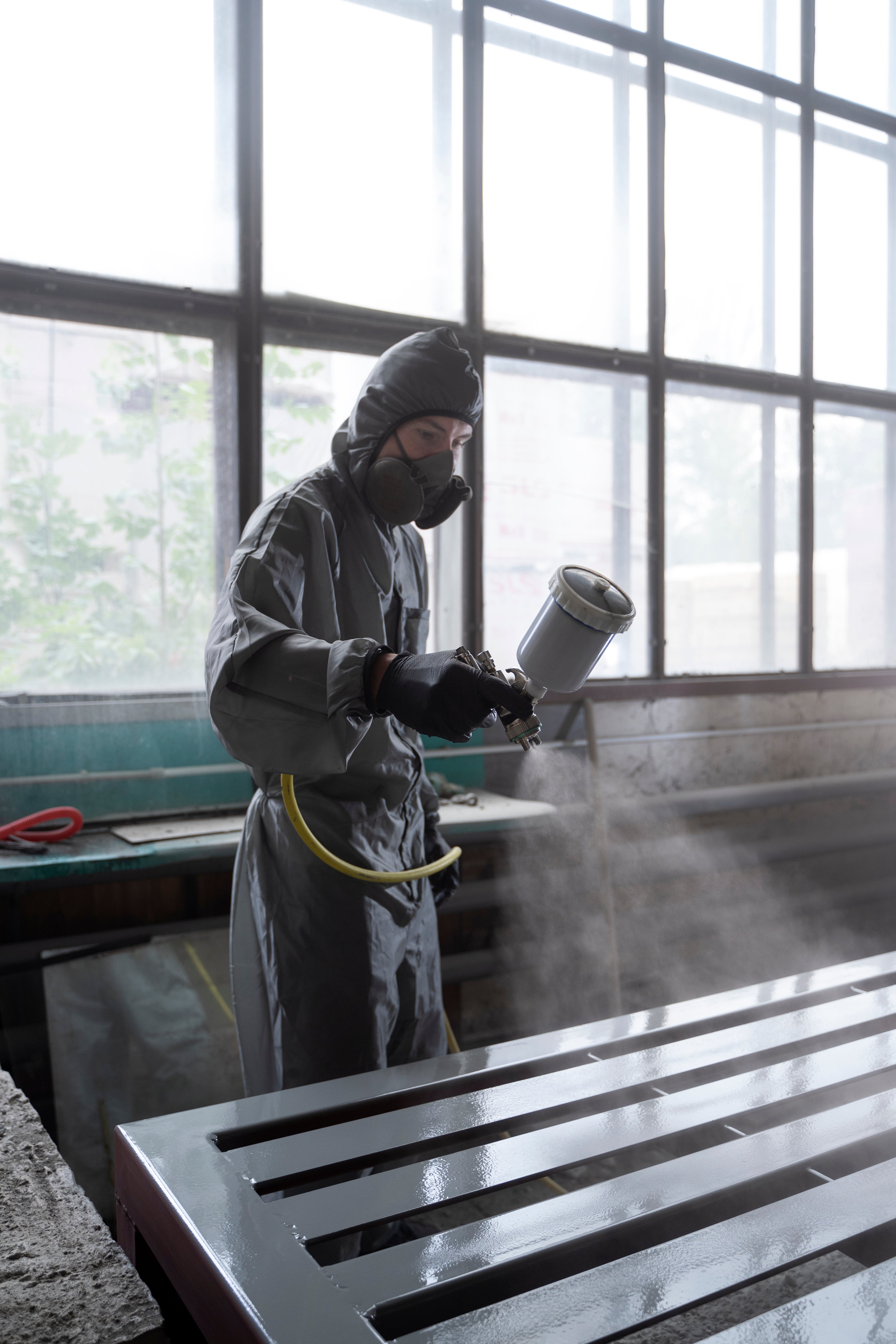 Travailleur portant des équipements de protection pour sablage en train de pulvériser une surface métallique dans un atelier